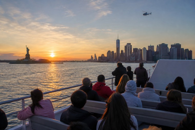 A sightseeing cruise boat passing the Statue of Liberty at sunset in New York Harbor